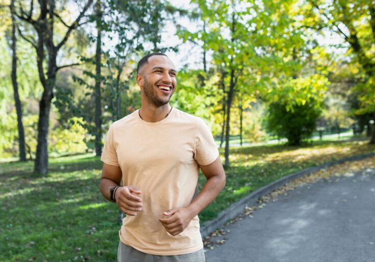 Cheerful and successful hispanic man jogging in the park, man running on a sunny day, smiling and happy having an outdoor activity.